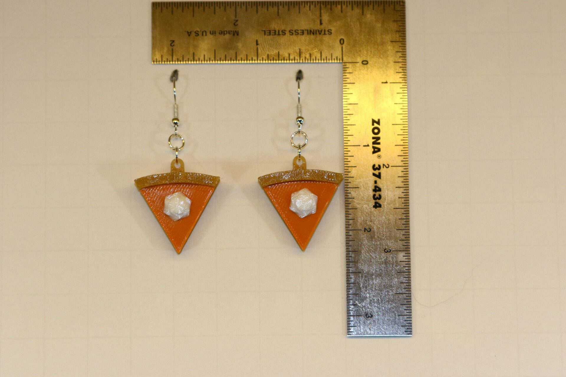 Pair of earrings shaped like a slice of pumpkin pie with golden crust and orange filling.
