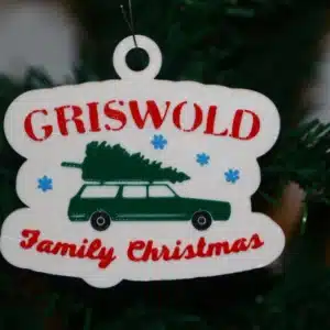 Griswold Christmas ornament featuring car with tree on roof, colorful holiday design.
