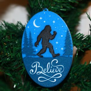 Bigfoot Christmas ornament with forest background, silhouette, and “Believe” text.