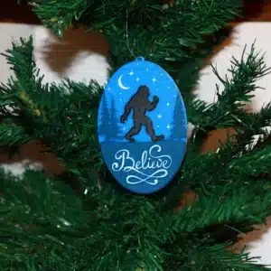 Bigfoot Christmas ornament with forest background, silhouette, and “Believe” text.