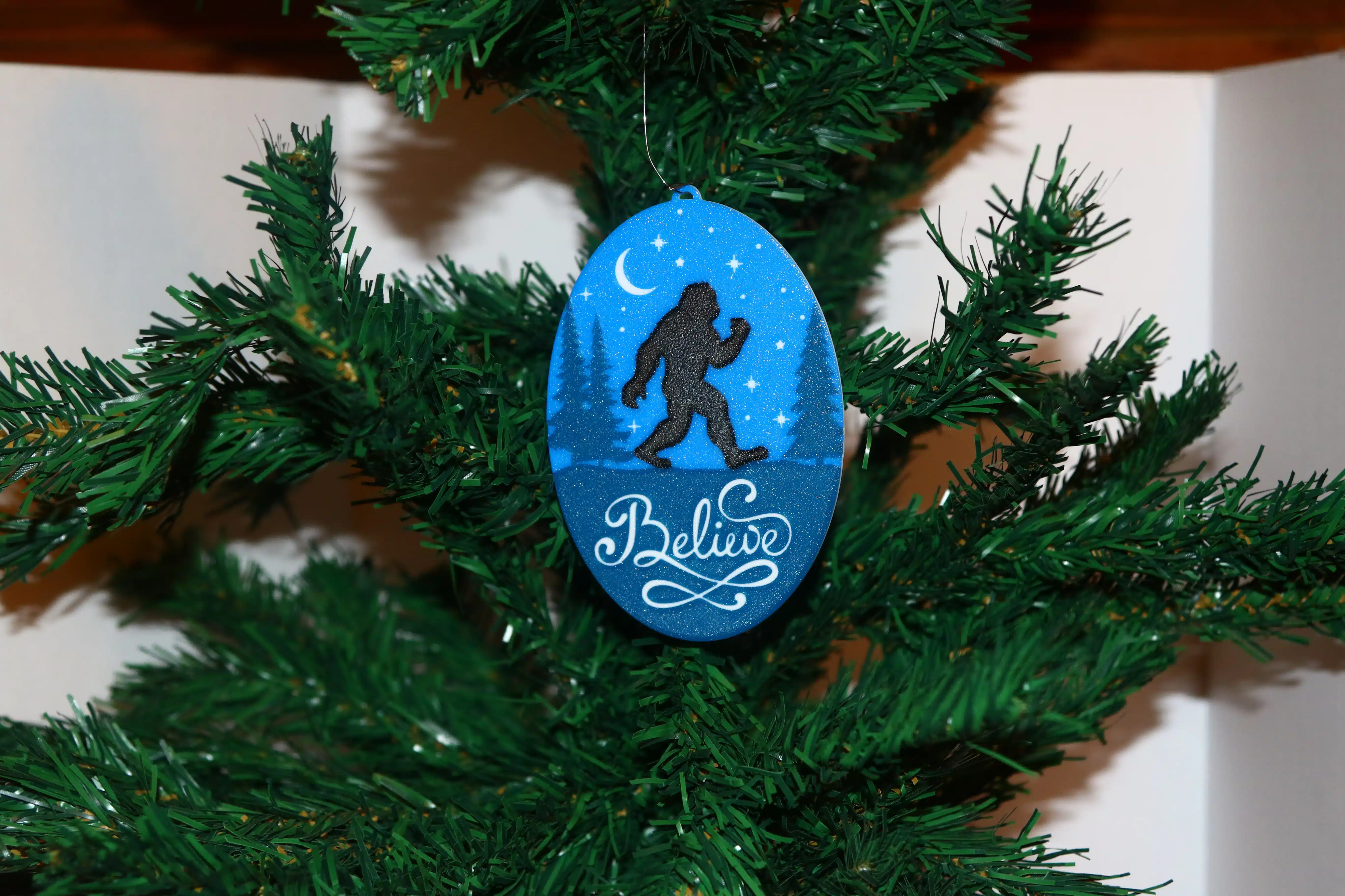 Bigfoot Christmas ornament with forest background, silhouette, and “Believe” text.