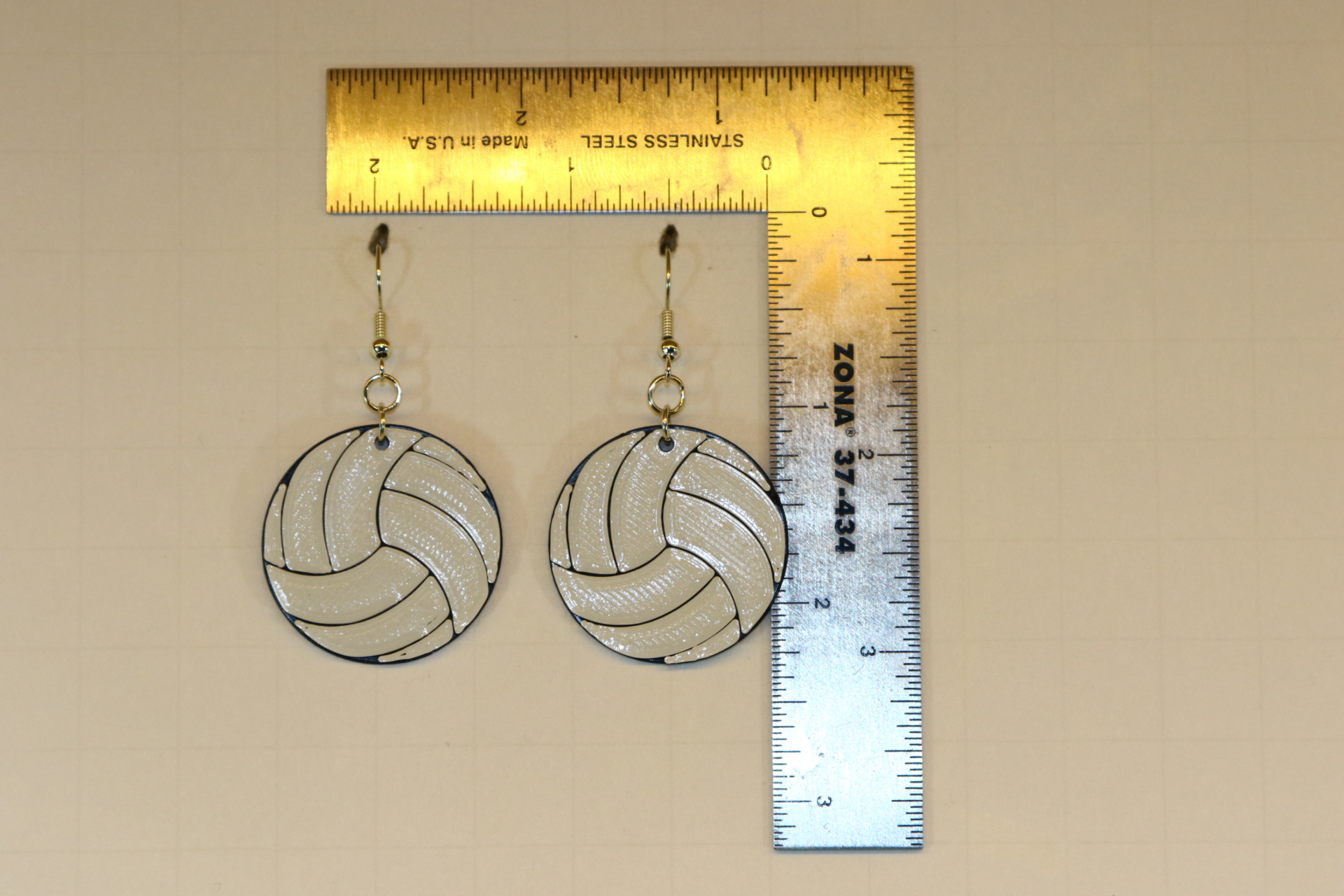 Pair of earrings shaped like a white volleyball with black lines.