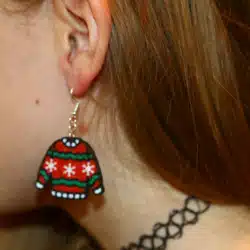 Pair of miniature ugly sweater earrings with colorful patterns.