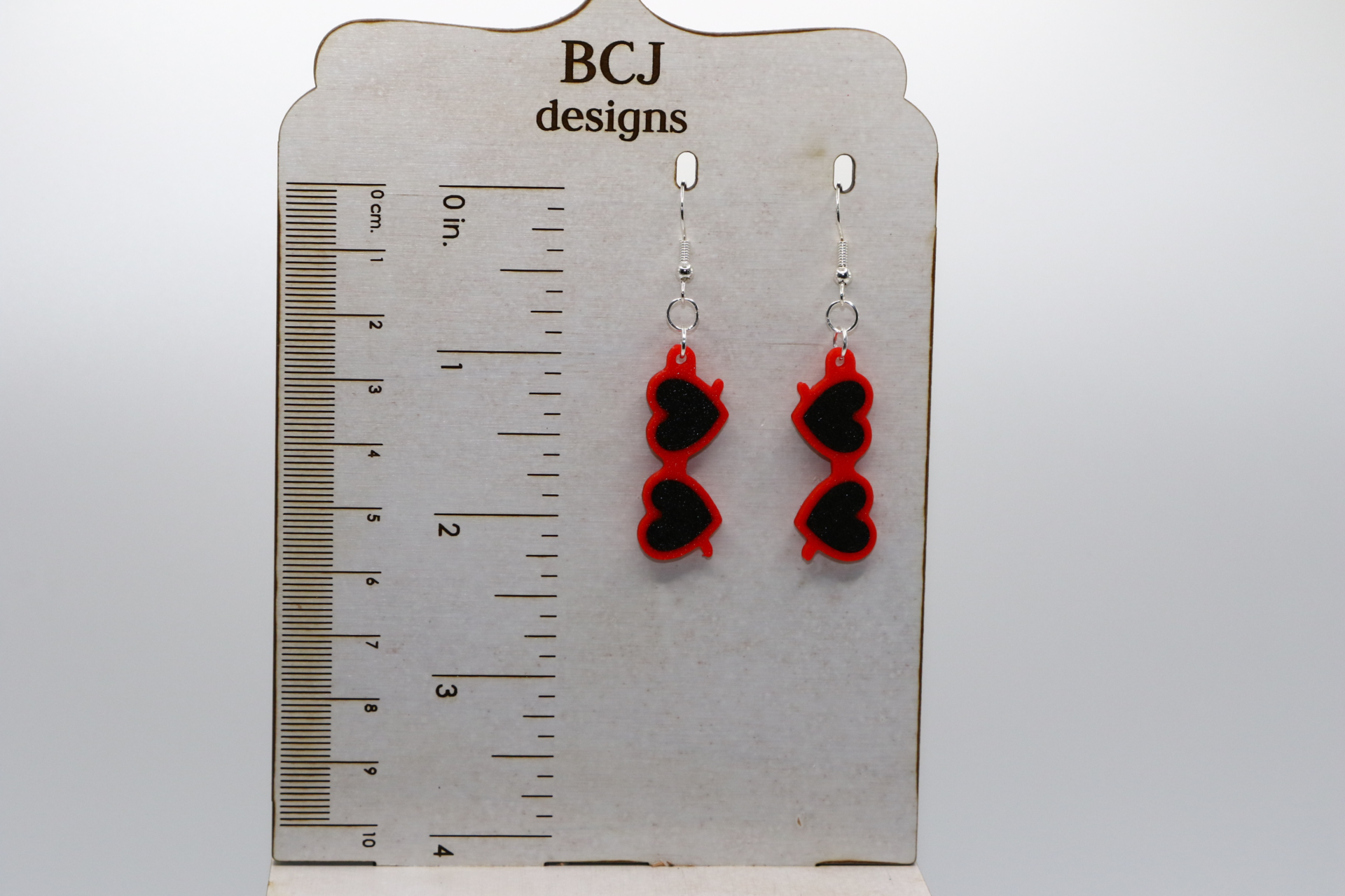 Pair of heart-shaped sunglasses earrings in bright red with silver hooks.