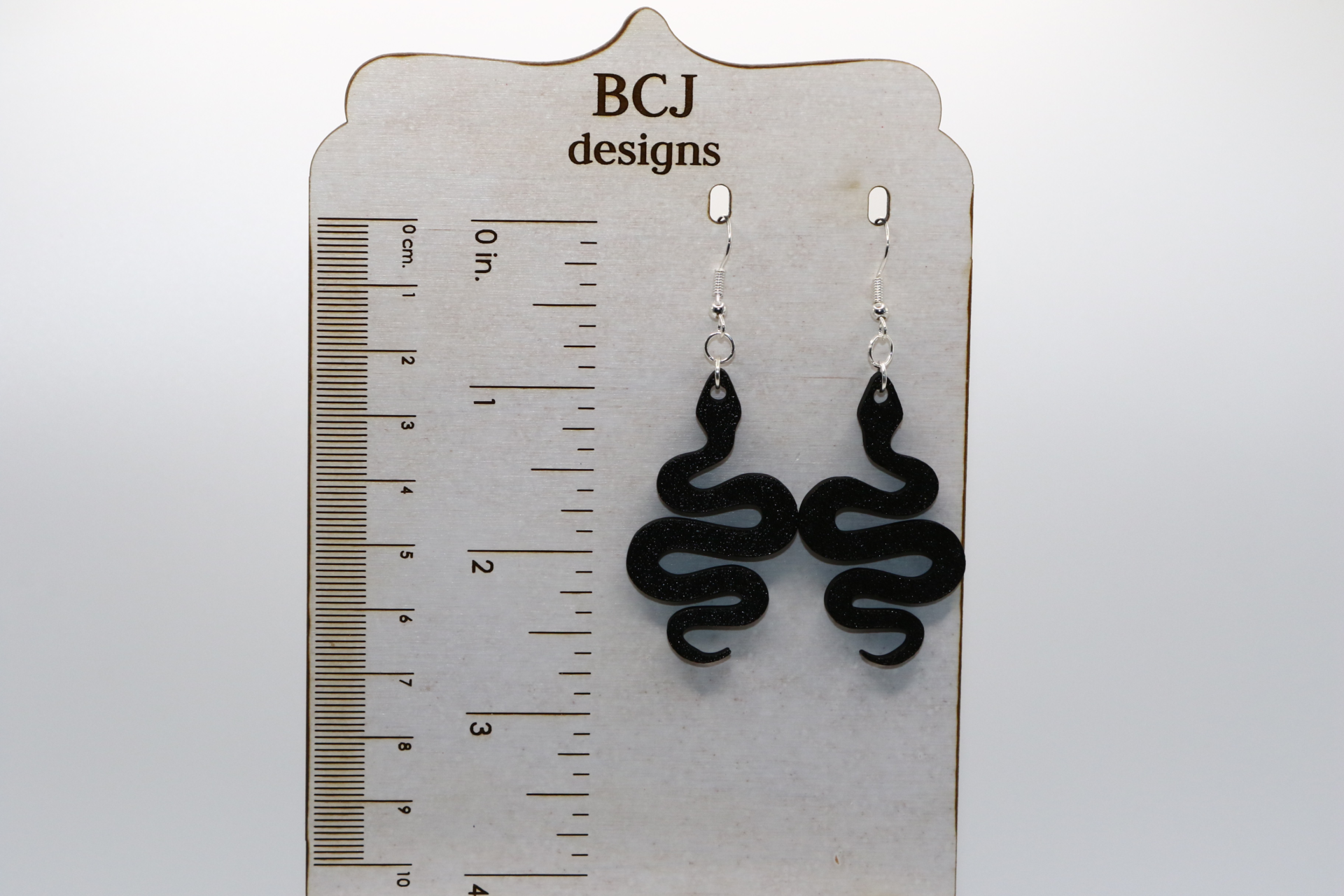 Pair of black snake earrings coiled with sleek detailing and silver hooks.