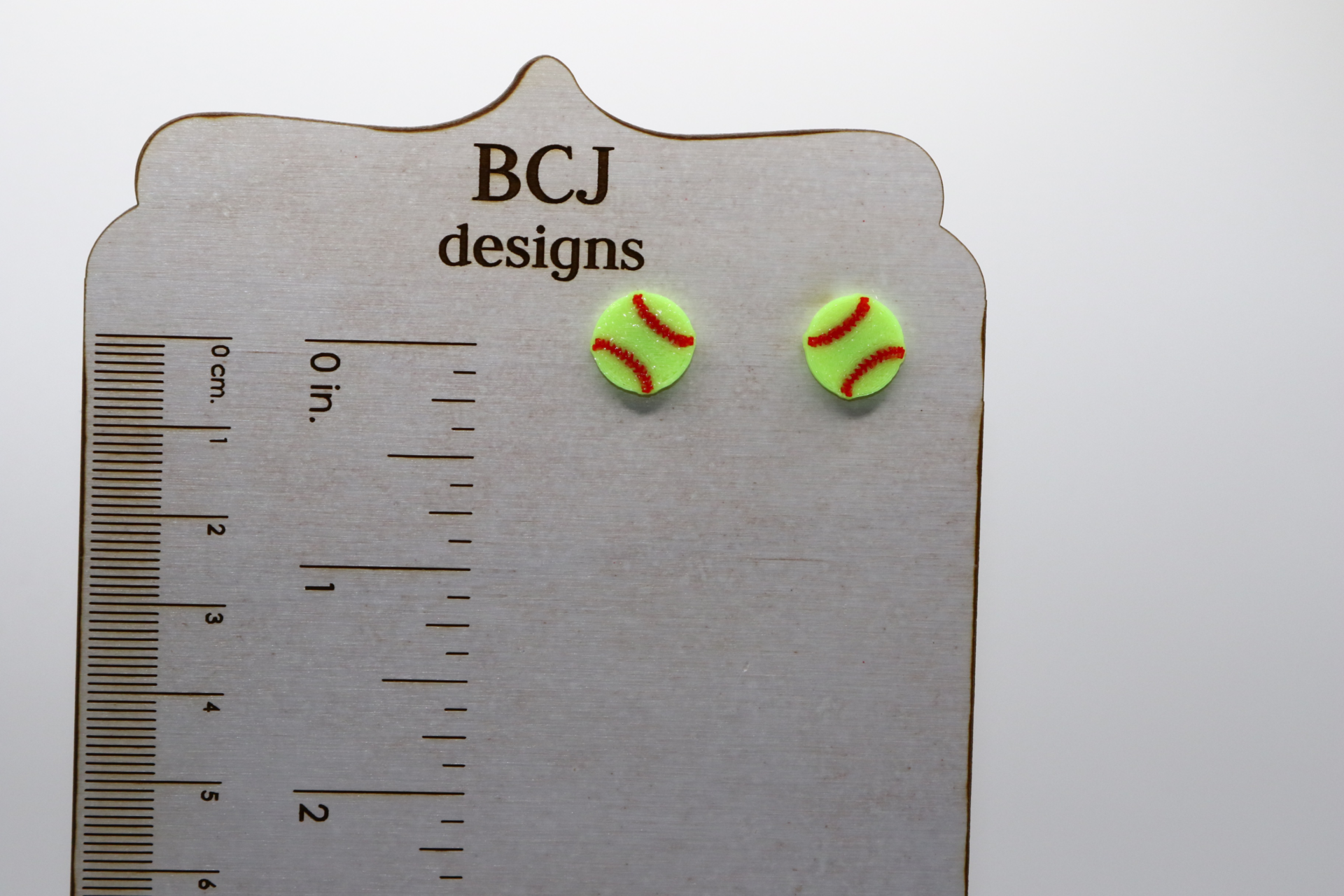 Pair of small stud earrings shaped like a yellow softball with red stitching.