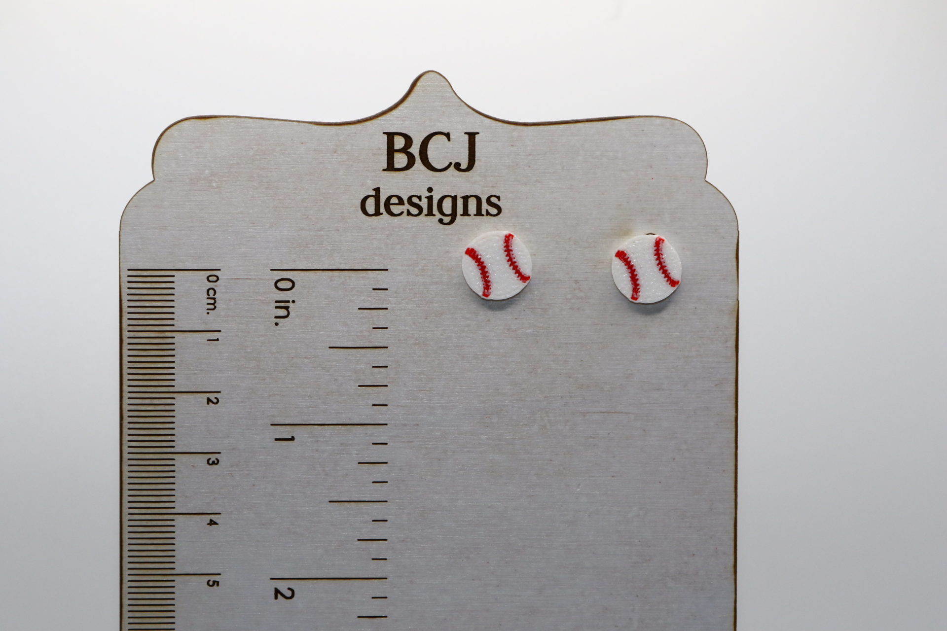 Pair of small stud earrings shaped like a baseball with red stitching.