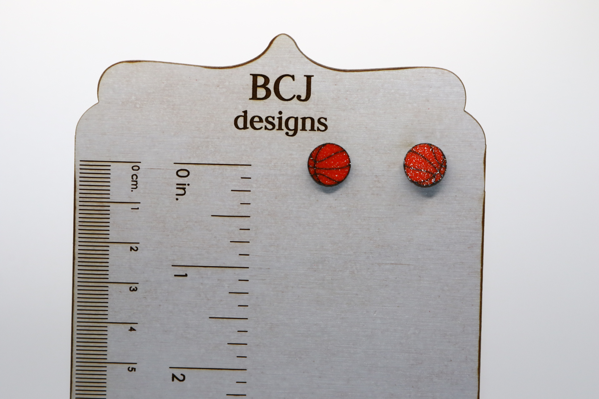 Pair of small stud earrings shaped like an orange basketball with black lines.