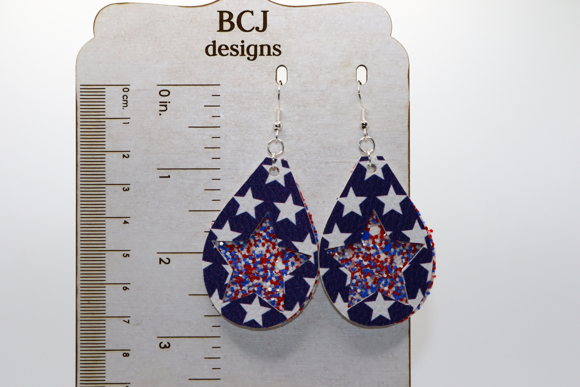 Pair of glittery red, white, and blue star earrings with silver hooks.