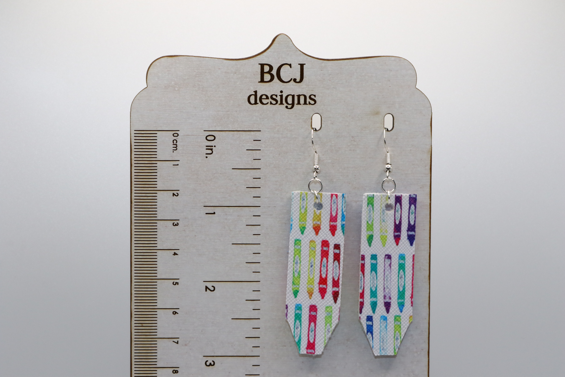 Pair of earrings shaped like colorful faux leather pencils with silver hooks.
