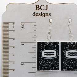 Pair of earrings shaped like black-and-white composition notebooks with silver hooks.