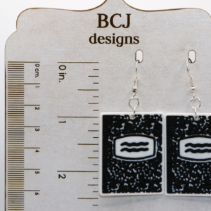 Pair of earrings shaped like black-and-white composition notebooks with silver hooks.