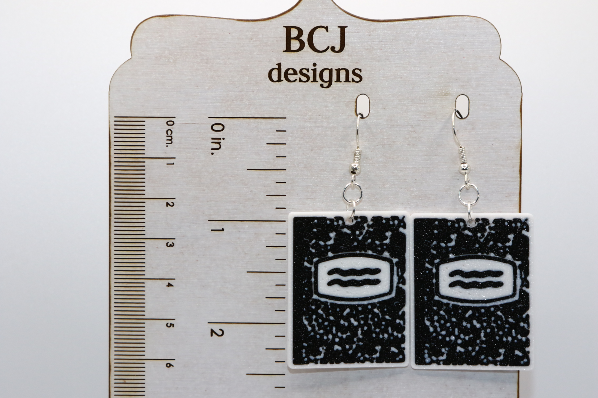 Pair of earrings shaped like black-and-white composition notebooks with silver hooks.