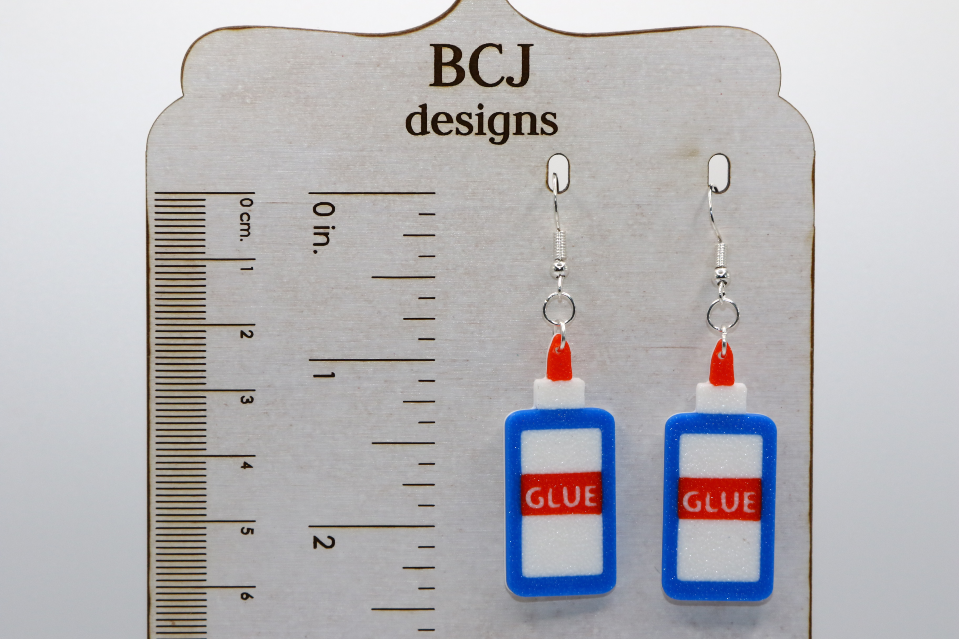 Pair of earrings shaped like a classic glue bottle with white and red details.