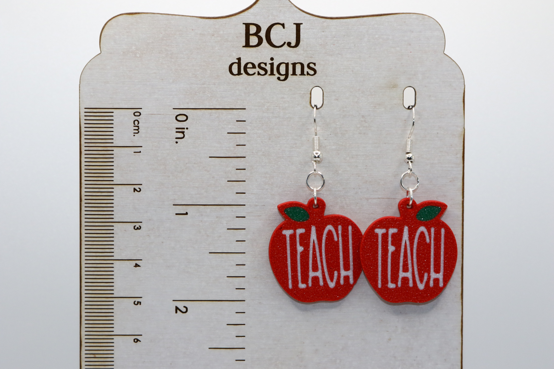 Pair of earrings shaped like red apples with the word “Teach” in white lettering.