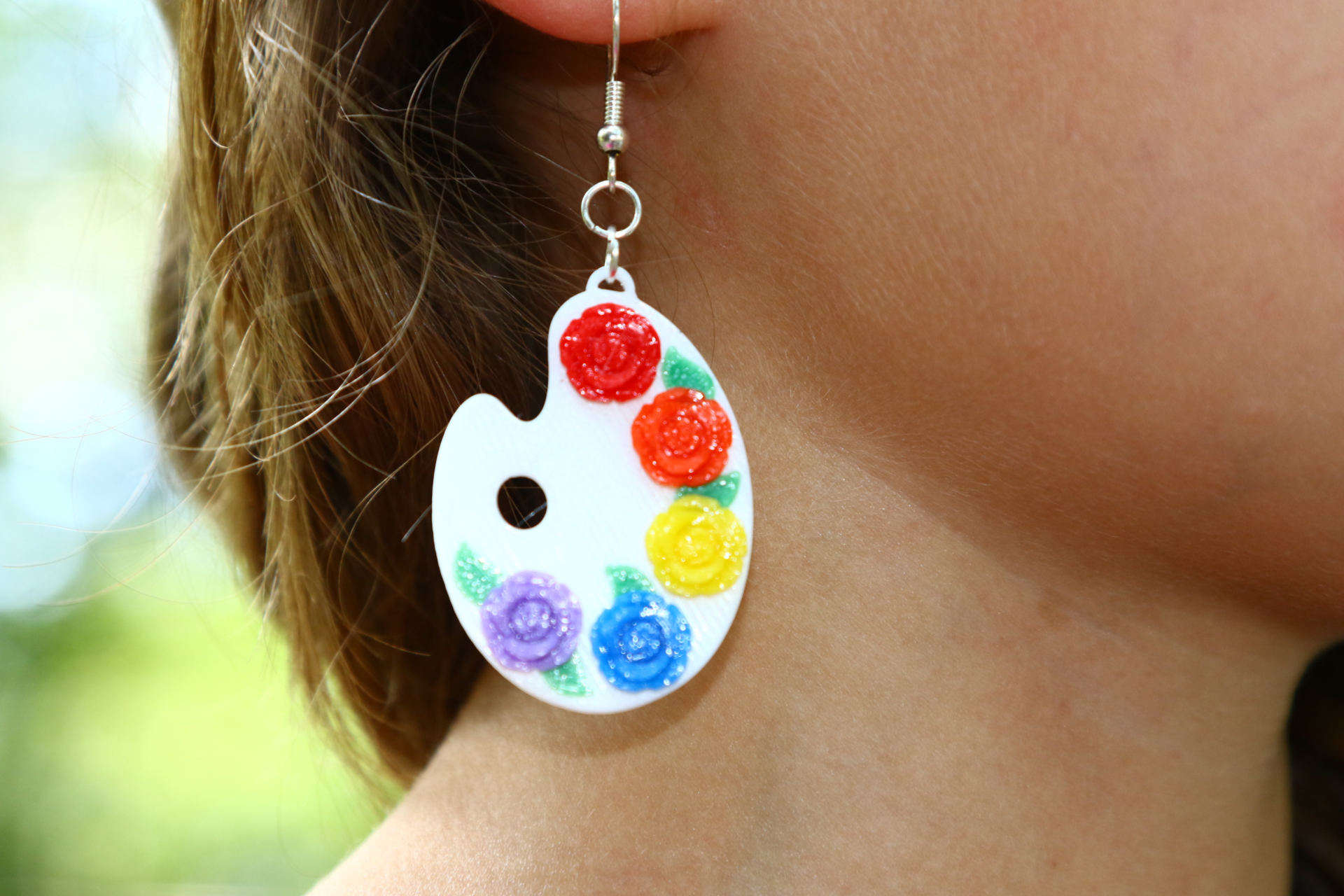 Pair of earrings shaped like painter palettes with multiple colorful paint spots.