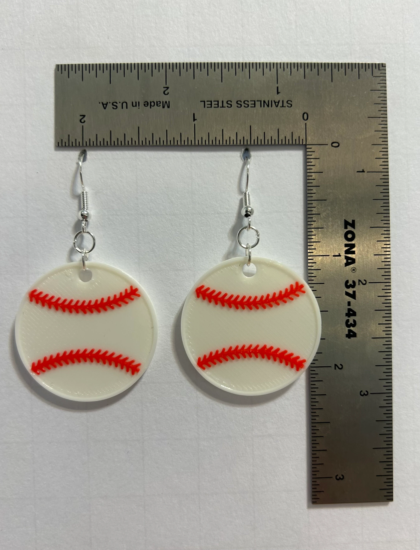 Pair of earrings shaped like a white baseball with red stitching.