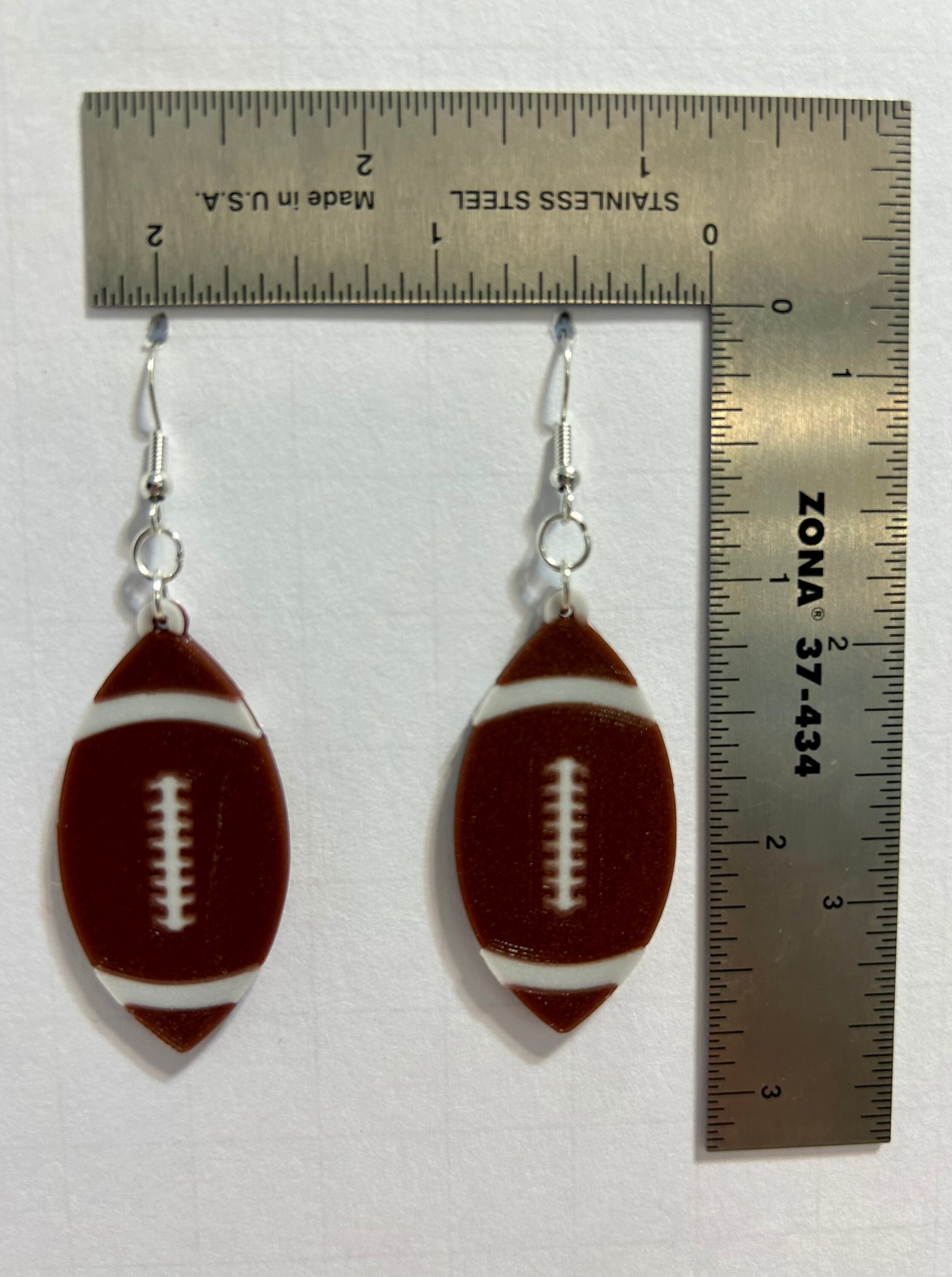 Pair of earrings shaped like a brown football with white stitching.