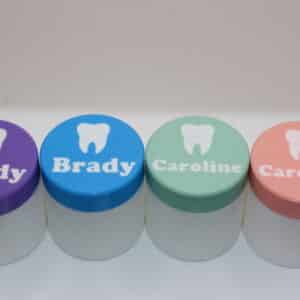 Personalized Tooth Fairy Boxes with white containers and custom colored lids featuring children's names and a raised tooth design in purple, blue, mint green, and pink.